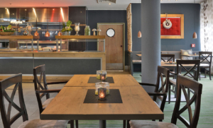 Leerer Restaurantbereich mit Holzstühlen und langen Tischen.