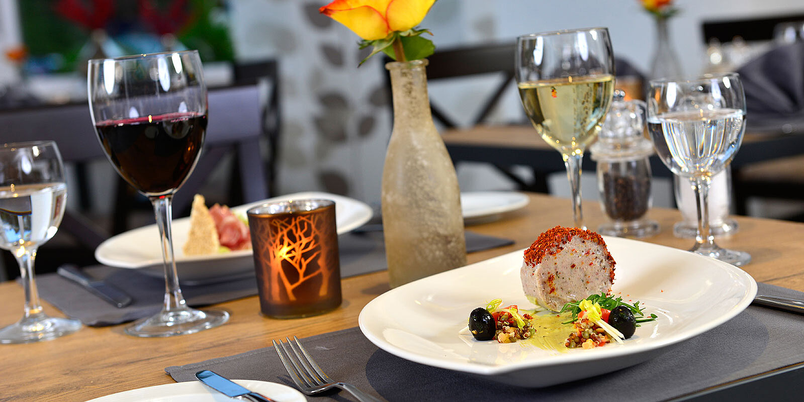 Tellergericht mit Wein und Blumenvase auf festlich gedecktem Tisch