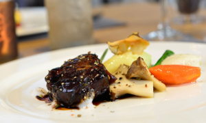 Hauptgericht mit Fleisch, Wurzelgemüse und Pilzen auf weißem Teller.