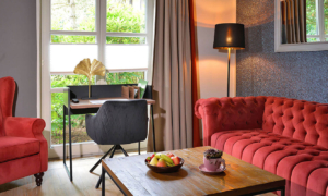 Suite_5_6645e5c8b4 Sitzgruppe mit rotem Sofa, Stehlampe und Fensterblick