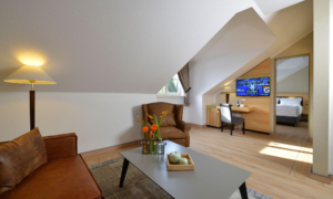 Landhotel_Schnuck-Heideland-Suite-0822_02 Dachzimmer mit Sofa, Couchtisch und Blick auf das Bett