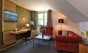 Stilvoller Wohnbereich mit rotem Samtsofa, Sessel, Schreibtisch und TV in warm beleuchtetem Raum.