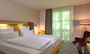 Modernes Hotelzimmer mit Doppelbett, gelbem Kopfteil, großem Fenster und warmem Licht.