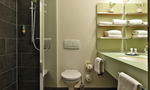 Modern, compact bathroom with a shower, wall-mounted toilet, and light-colored vanity with a mirror and towels.