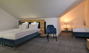 Attic room with three single beds, a small bedside table, and a warmly lit lamp beneath the sloping ceiling.