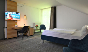 Modern hotel room with a large bed, desk, wall-mounted TV, and seating area by the window.